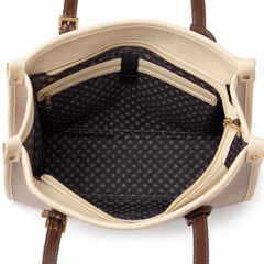 Open view of a tote bag showing the cream-colored exterior, brown leather handles, and a dark patterned interior lining with a zippered pocket.